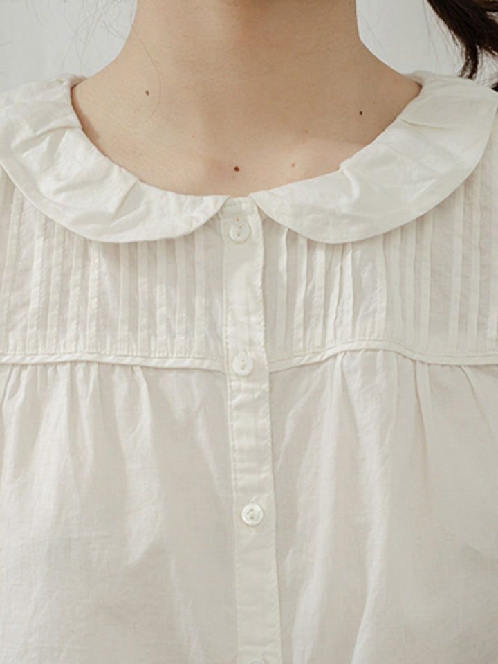 モデルがフランス少女プリーツ付きフリルスリーブレス白コットンシャツを着用し、エレガントなスタイルを披露。