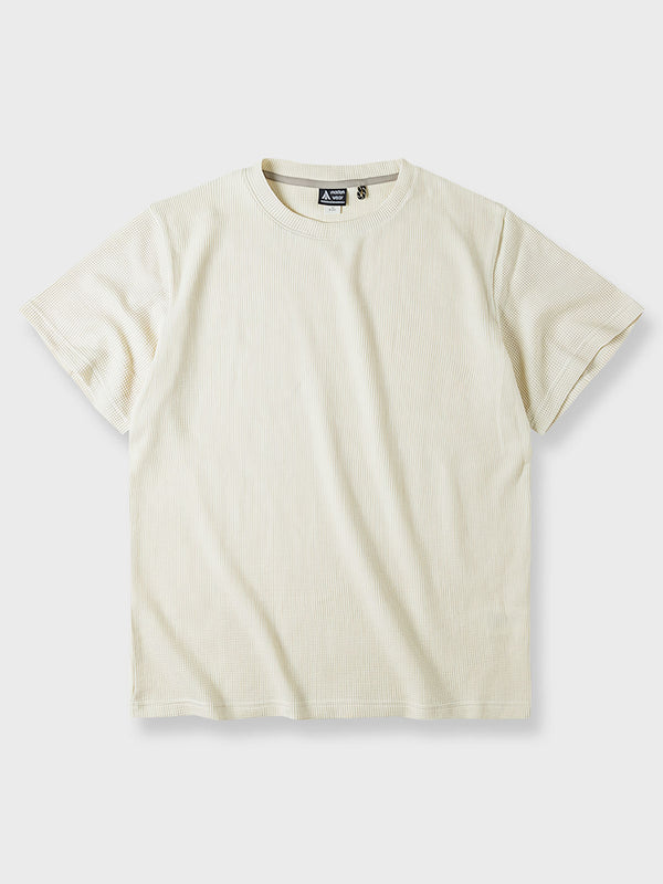 クラシックなワッフル織りパターンのニットTシャツ。中性的なベージュ色で、凹凸のあるテクスチャーが特徴。