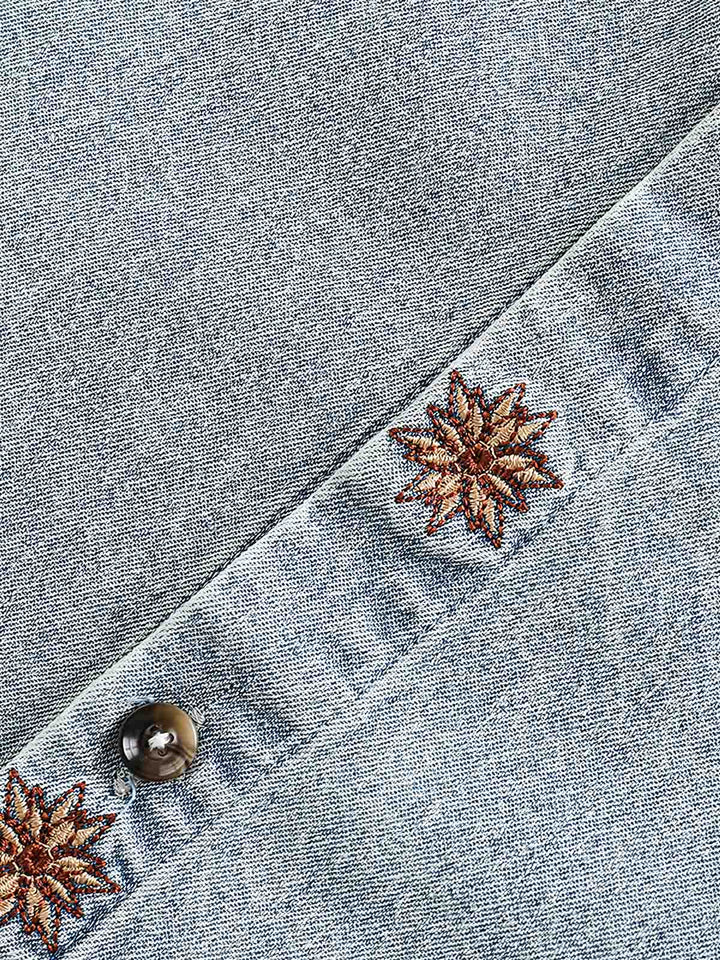 シャツの洗練された刺繍パターンのクローズアップ。デニム素材とウォッシュ加工が西部のカウボーイ服の歴史を反映し、現代的なデザインを取り入れています。