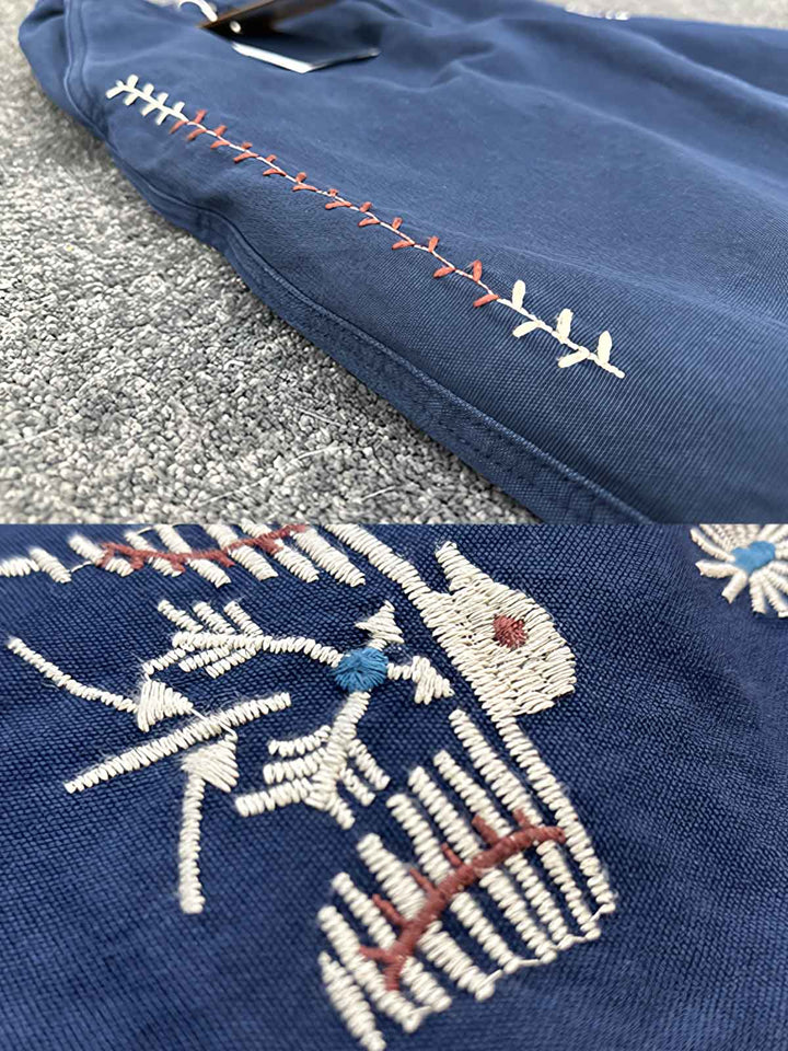 カジュアルパンツに施された雷鸟の刺繍のクローズアップ。シンプルながら深い意味を持つデザインで、自然界への敬意を表しています。
