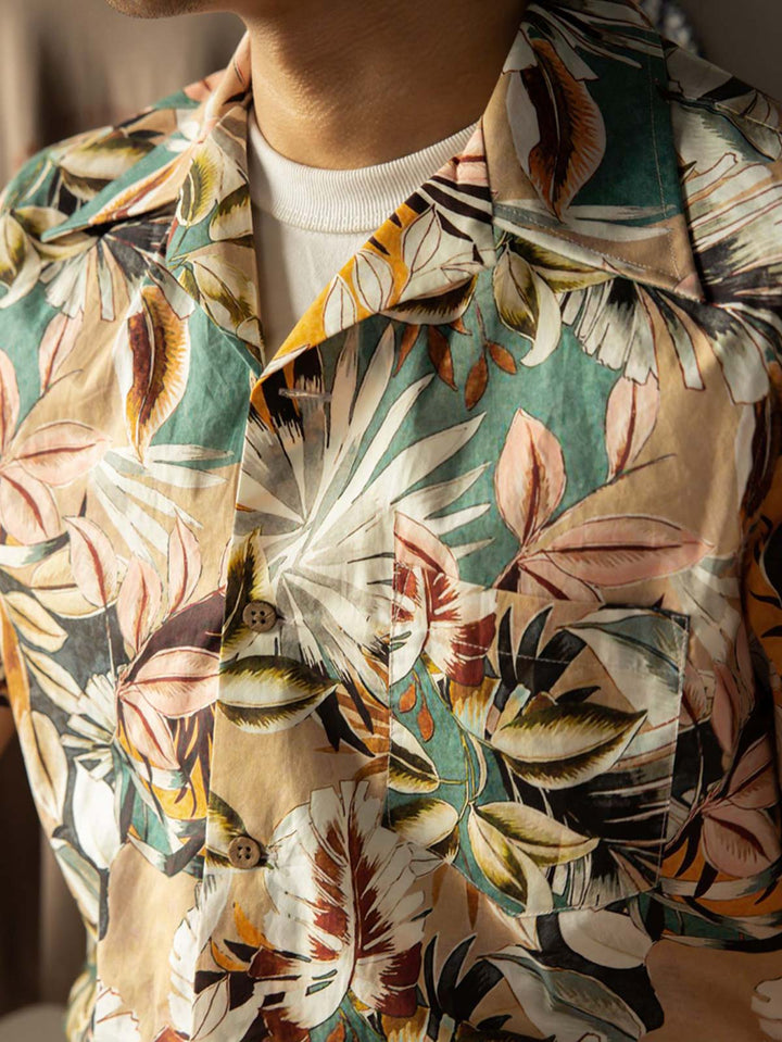 モデルがハワイアンプリント半袖シャツを着用し、無地のカジュアルパンツとシンプルなサンダルを合わせたスタイルでポーズ。明るく夏らしいカジュアルスタイルを演出。