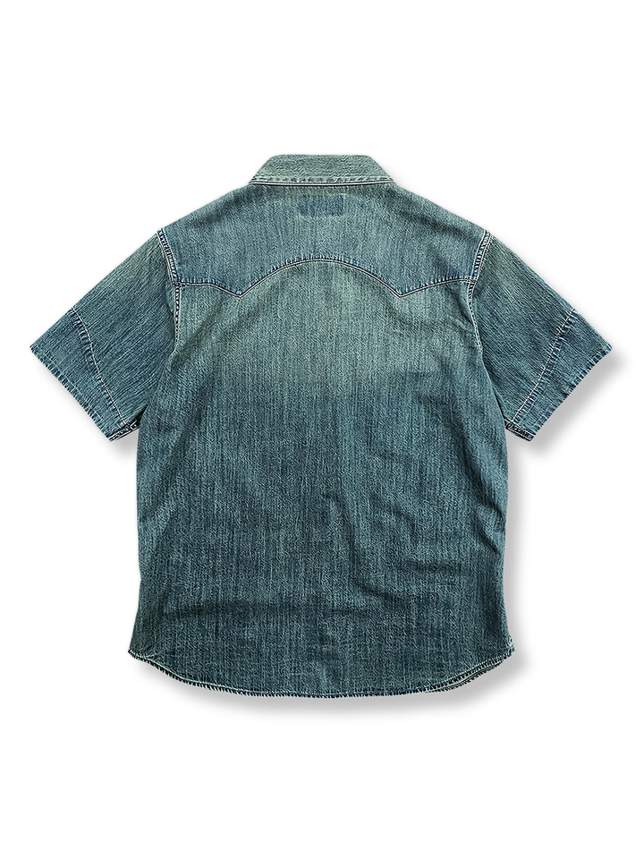 ウェスタンスタイルのデニム半袖シャツの正面ビュー。典型的なダブルポケットと精密なステッチワークが特徴で、アシンメトリックな裾とサイドスリットが加えられたモダンなデザインです。