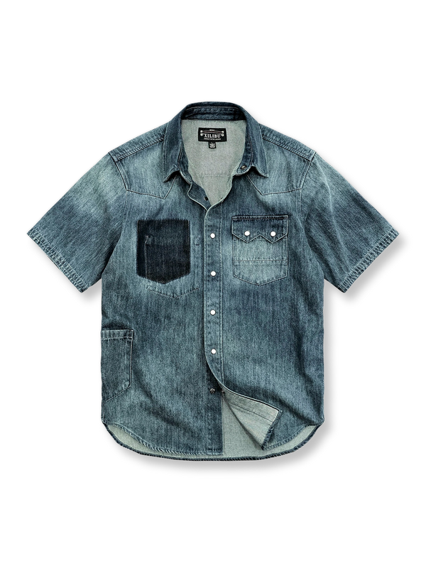 レトロなウォッシュとブリーチ処理が施されたパッチポケット付きのデニム半袖シャツの正面ビュー。ゆったりとしたストレートフィットで、肩部分にパッチデザインと貝殻ボタンが特徴的です。