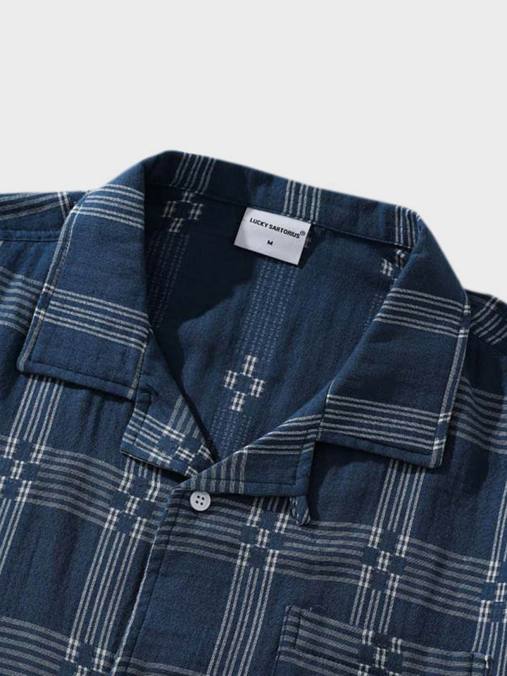 チェック柄キューバンカラーシャツの細部、特に精緻に縫製されたポケットと洗練されたボタンディテールが特徴です。